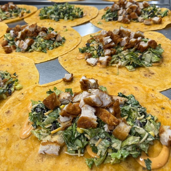 Multiple yellow tortillas filled with salad, black beans, corn, and fried chicken pieces.