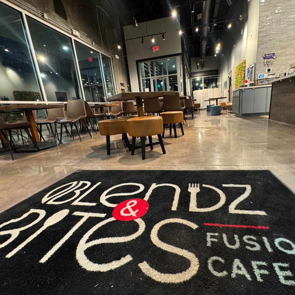 A wide shot of the Blendz & Bites Fusion Cafe interior with tables, chairs, and a welcome mat.
