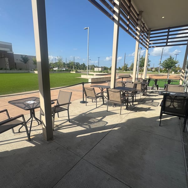 Outdoor patio with metal tables and chairs, overlooking a green lawn under a clear blue sky.