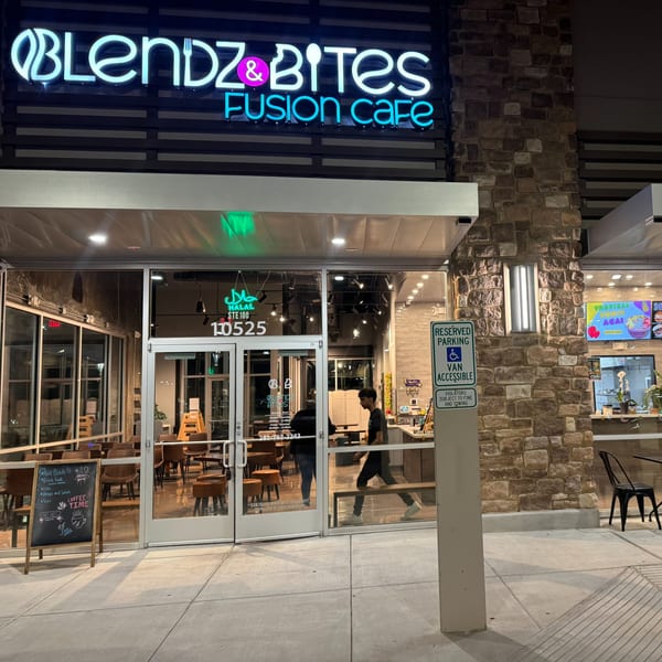 Exterior of Blendz & Bites Fusion Cafe at night, with neon signs and a person walking inside.