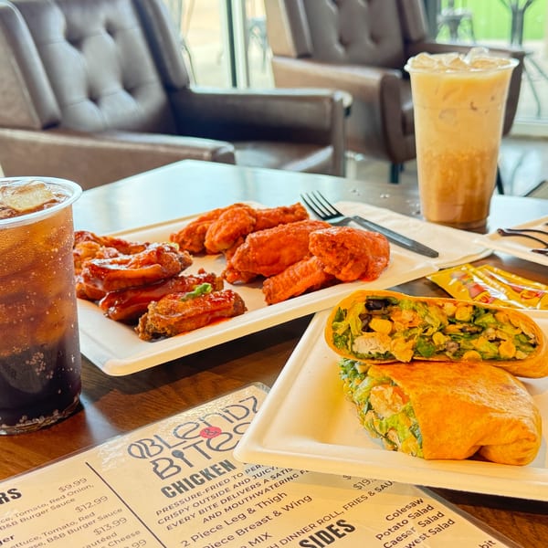 A table with chicken wings, a wrap, and two iced drinks, with a menu visible.