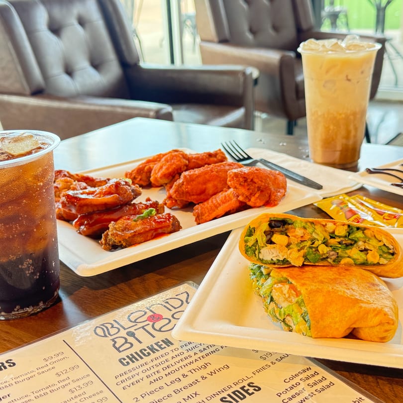 A table with chicken wings, a wrap, and two iced drinks, with a menu visible.