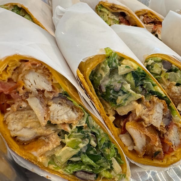 Several chicken wraps with lettuce, tomatoes, and sauce, partially wrapped in white paper.