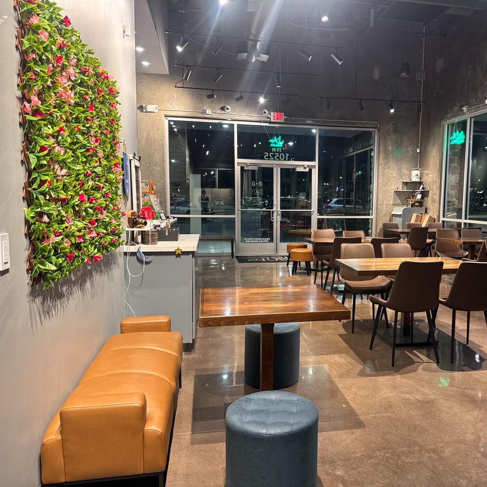 Modern cafe interior with a floral wall, wooden tables, brown chairs, and a large glass entrance.
