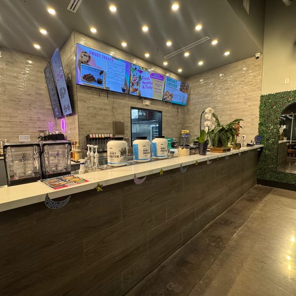 A modern restaurant counter with digital menus, blenders, protein powder, and decorative plants.