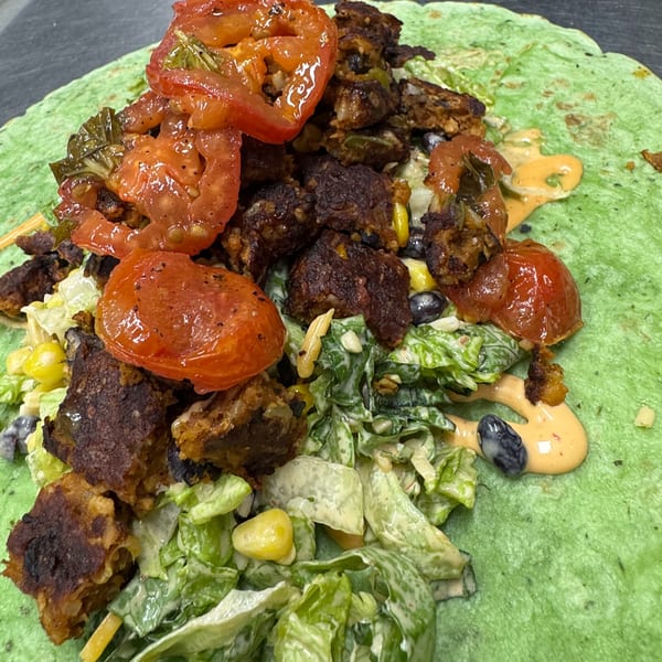 A vibrant green tortilla wrap filled with roasted tomatoes, dark meat, lettuce, corn, and black beans.