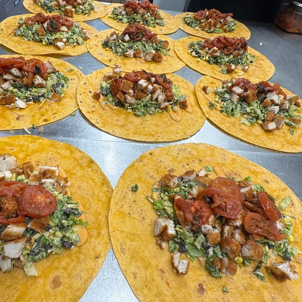 Multiple yellow tortillas filled with chicken, lettuce, black beans, corn, and tomatoes on a metal surface.