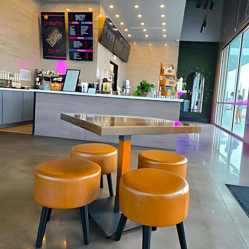 Modern cafe interior with orange stools around a square table, counter, and menu boards.