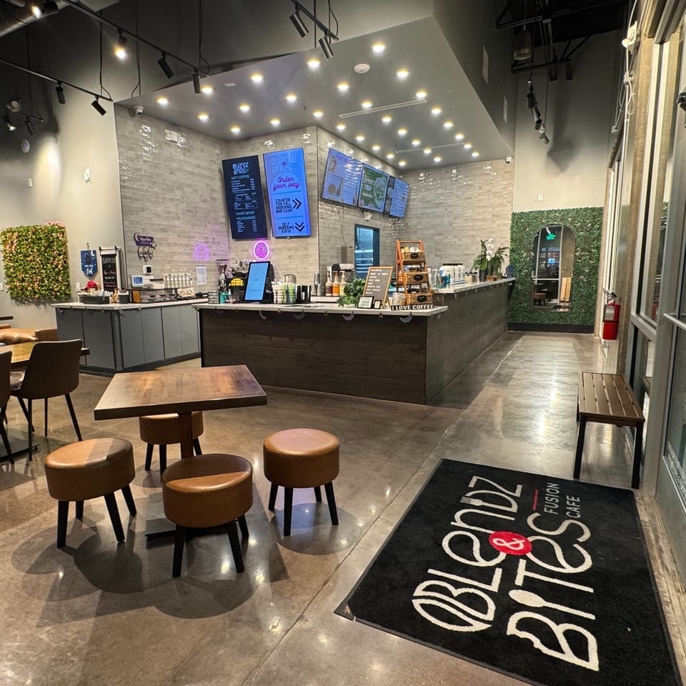 Interior of Blendz & Bites Cafe with a counter, menu screens, tables, and a welcome mat.
