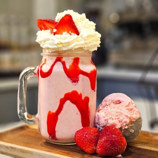 Strawberry milkshake in a mason jar with whipped cream, fresh strawberries, and a scoop of ice cream.