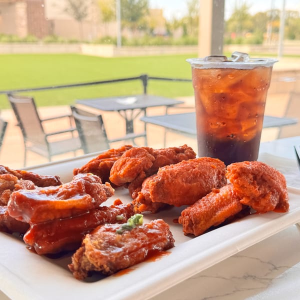 A plate of red-sauced chicken wings and an iced tea on a patio table with a grassy area.