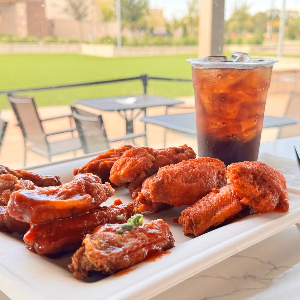 A plate of red-sauced chicken wings and an iced tea on a patio table with a grassy area.