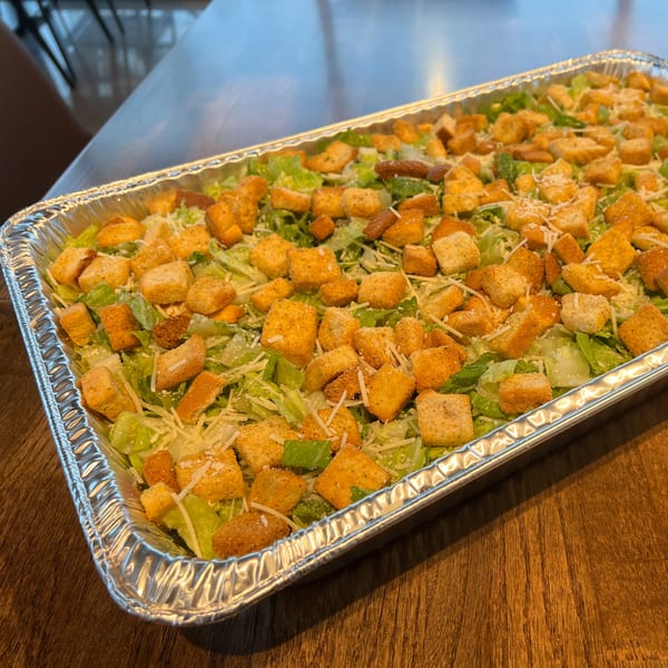 A large catering tray filled with fresh Caesar salad, topped with croutons and shredded cheese.
